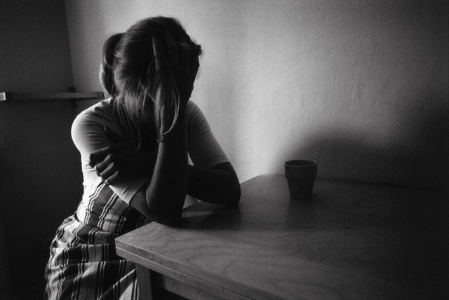 Female teenager sitting at table with head in hands